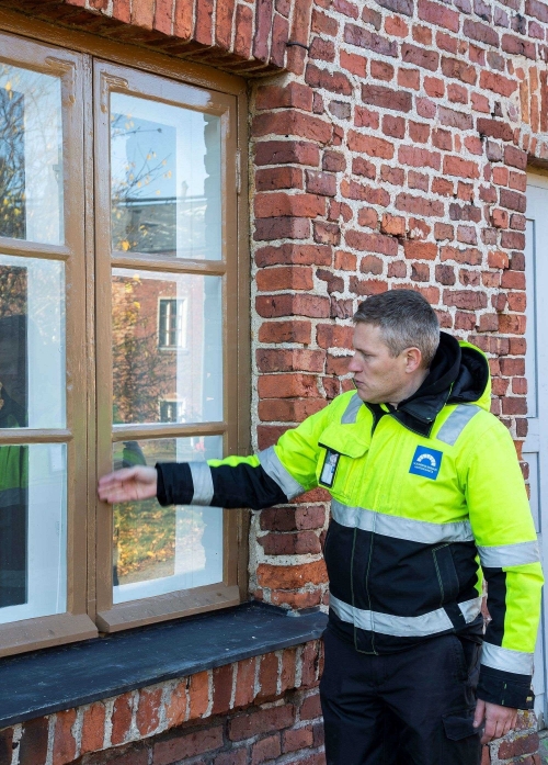 Henkilö työvaatteissa osoittaa ikkunaa.