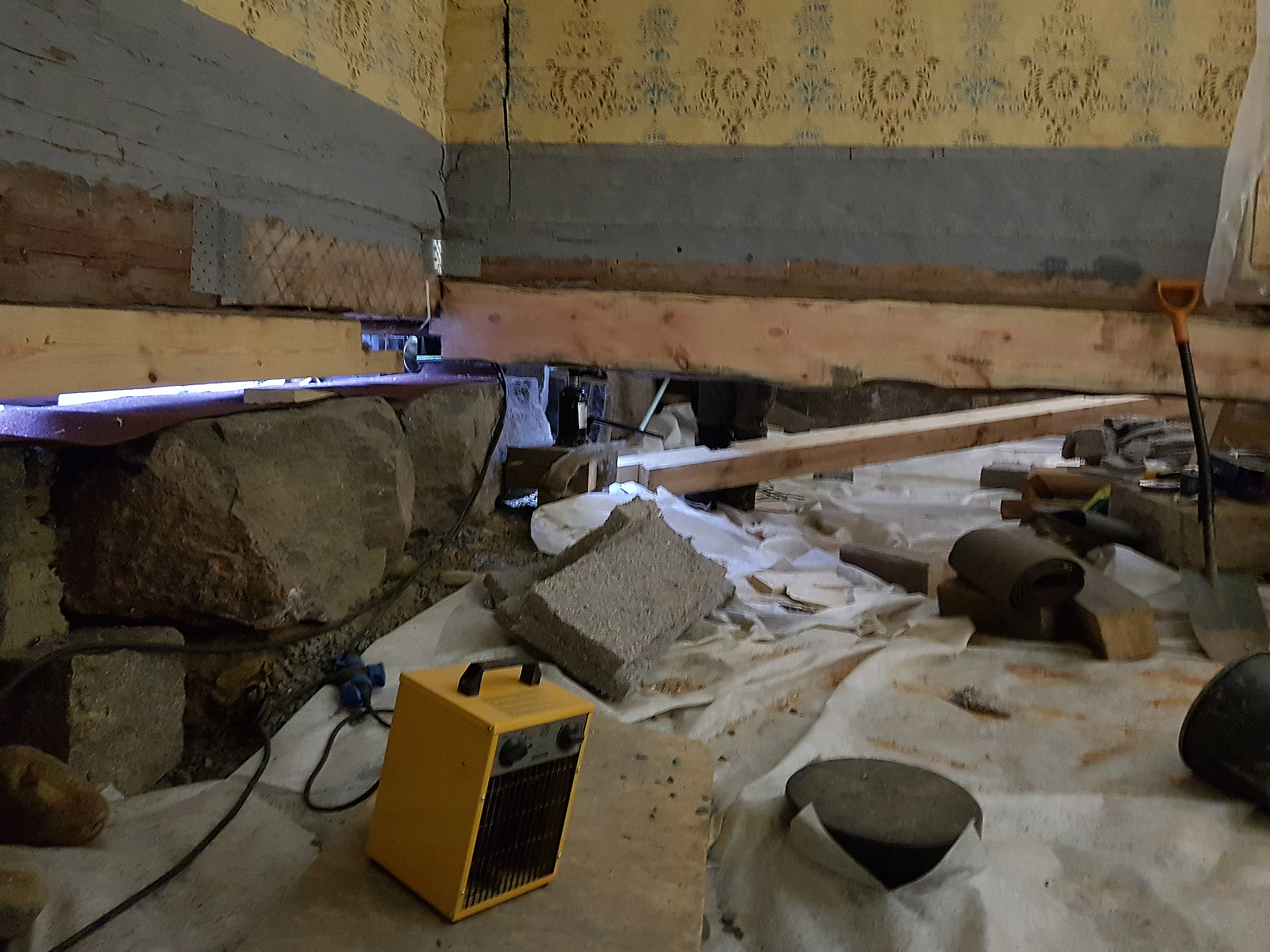 Ulkoseinän alimmaisen hirren alapuolella on paksu parru. Kivijalan ja parrun välissä on rako. Väliseinän alla on paksu uusi hirsi.