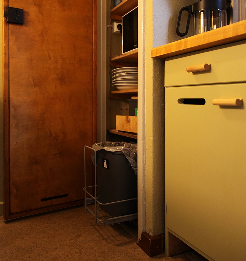 Kapeassa keittiönurkkauksessa näkyvät avoimessa kaapissa olevat avonaiset hyllyt kodinkoneineen ja astioineen.