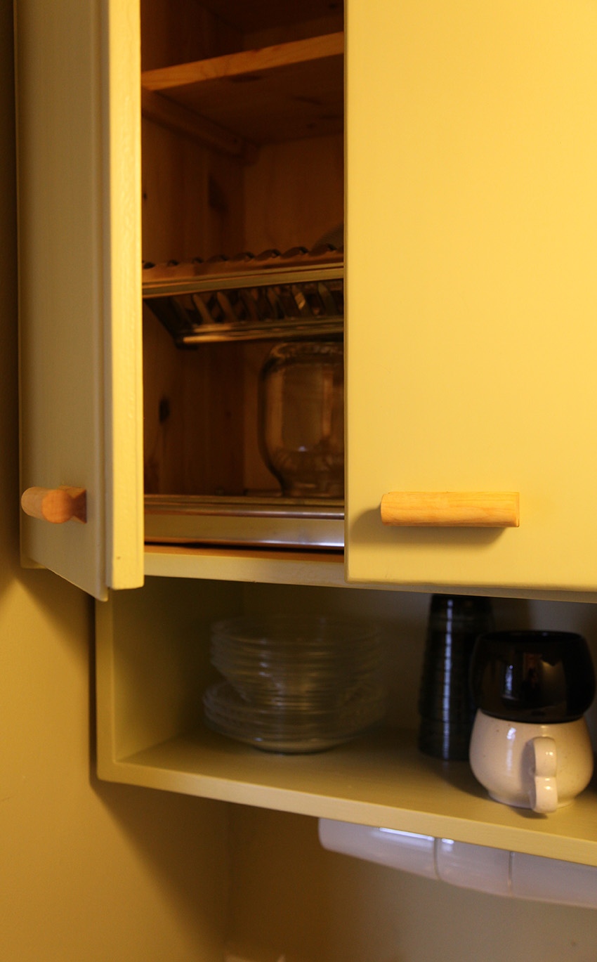 Avoinna oleva yläkaappi paljastaa metallisien kuivaustelineen, ja alla olevalla avohyllyllä on astioita.