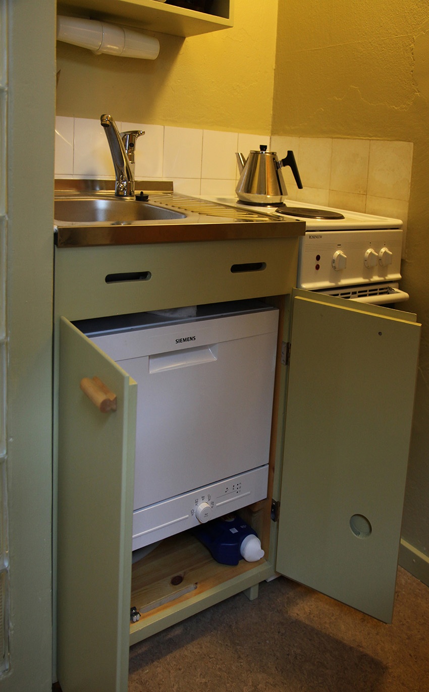 Keittiökaapin ovet ovat auki ja altaan alle sijoitettu kodinkone näkyy esillä.