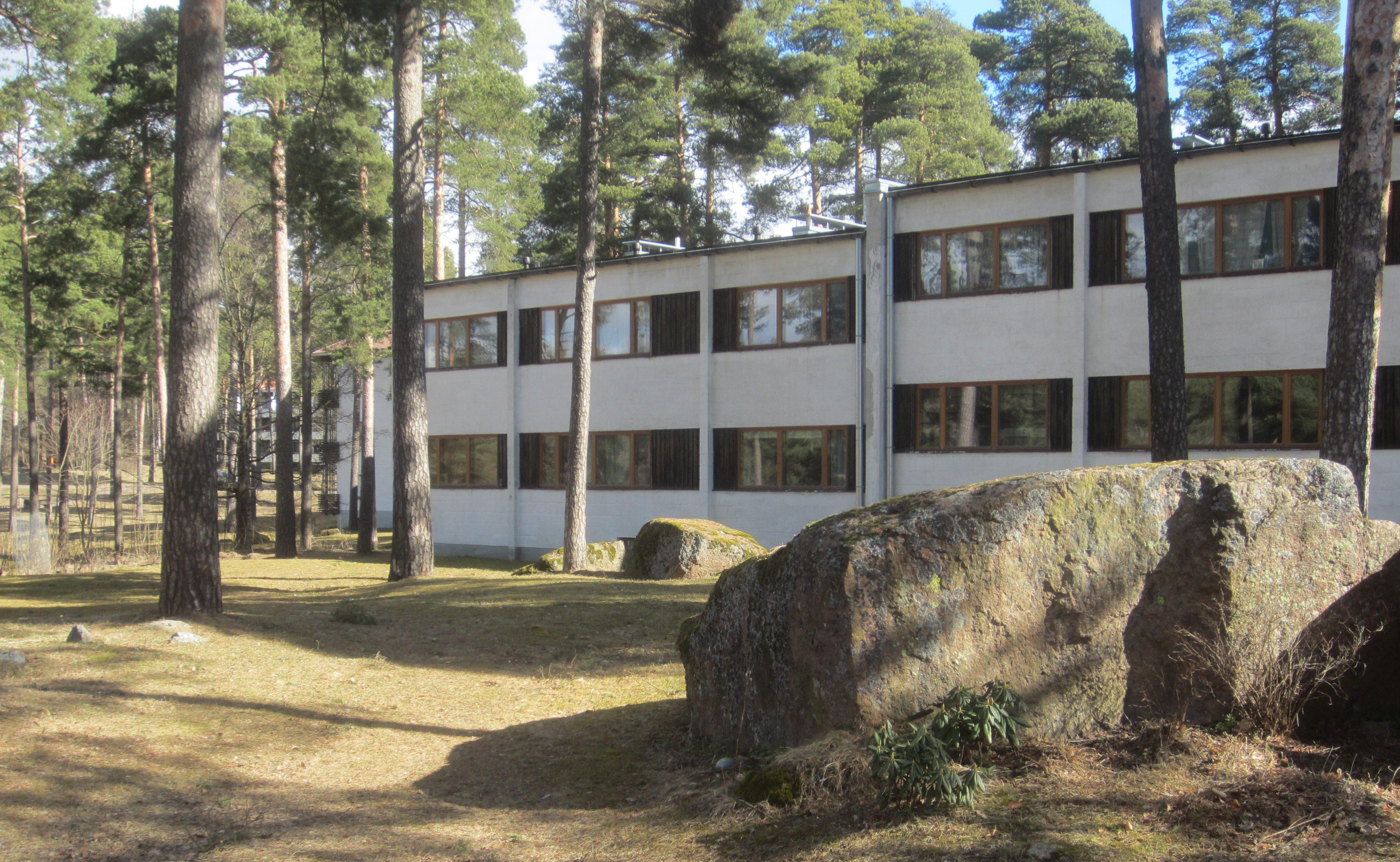 Valkea kaksikerroksinen asuinkerrostalo mäntyjen lomassa.